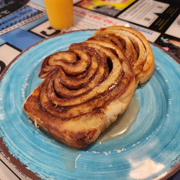 A Southside Diner cinnamon roll with glaze on a blue plate, with orange juice in the background.
