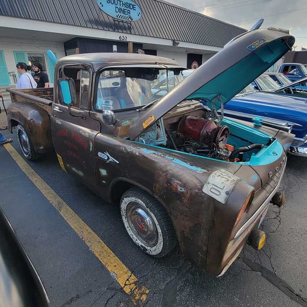 A rusty brown vintage pickup truck with its hood open, parked outside Southside Diner.