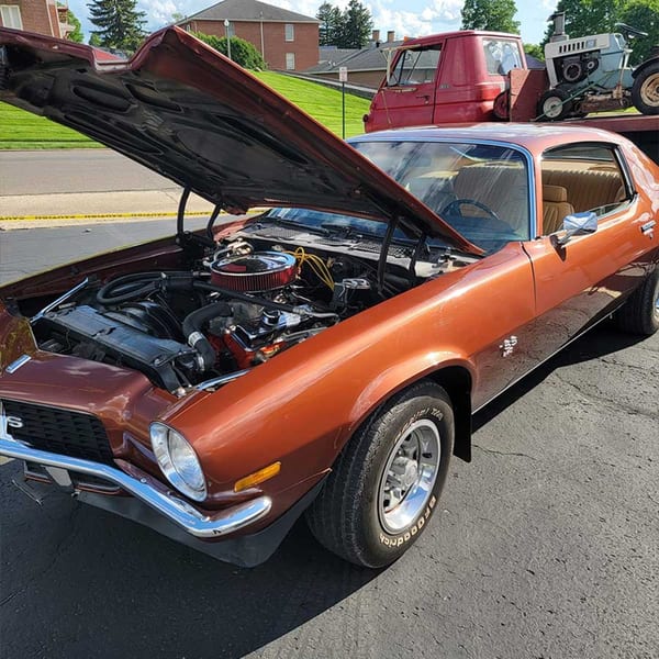 A classic bronze muscle car with its hood open, revealing the engine, parked outdoors.