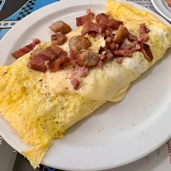 A Southside Diner omelet filled with cheese, topped with diced ham and sausage on a white plate.