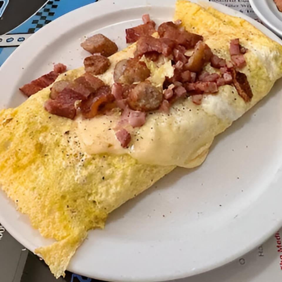 A Southside Diner omelet filled with cheese, topped with diced ham and sausage on a white plate.